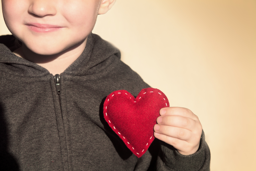 Un niño sujetando un corazón de lana junto al pecho